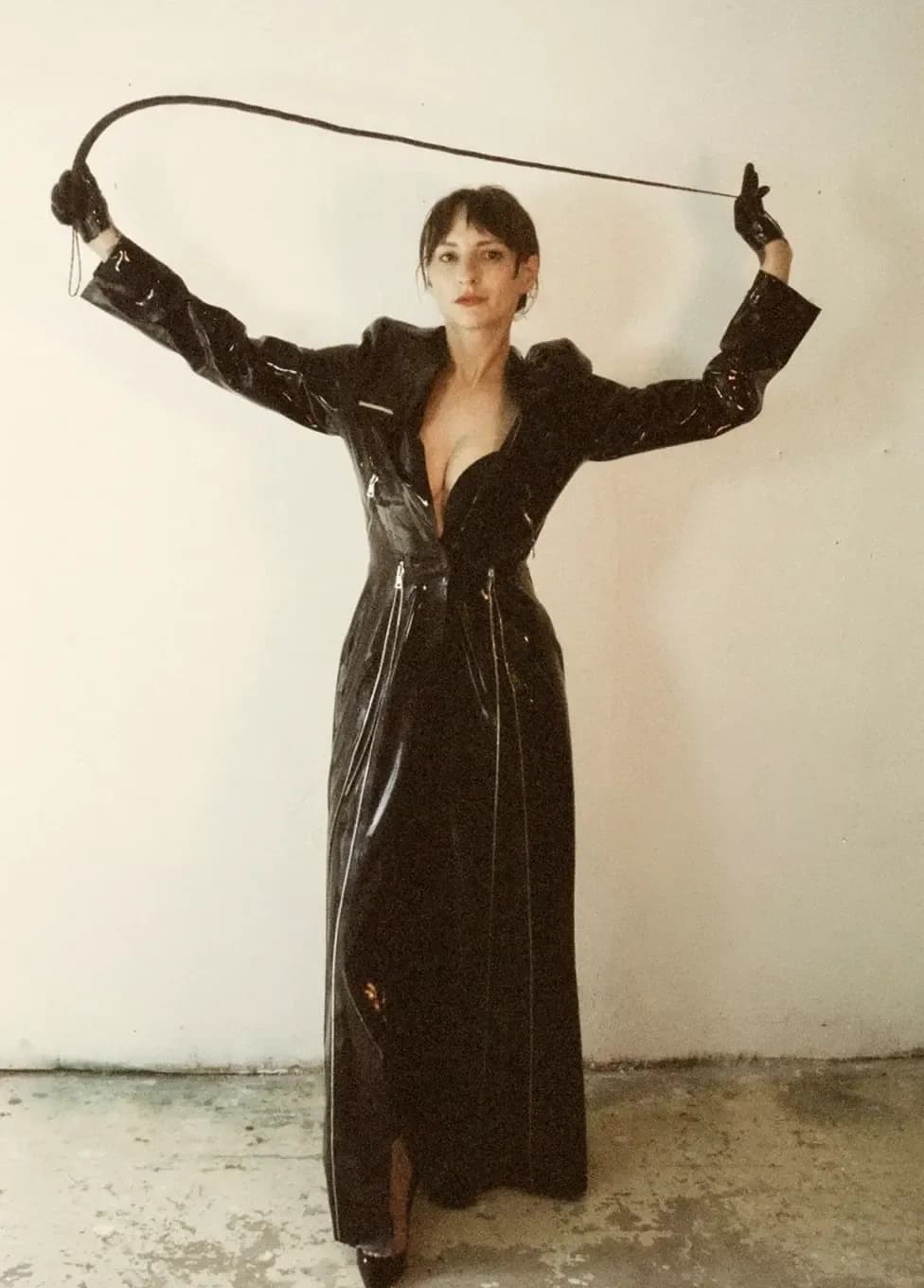 Woman in a long black latex coat holding a whip overhead